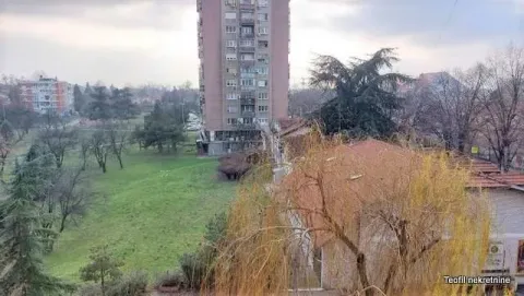 View from the window overlooking surrounding buildings and green area. - image 10