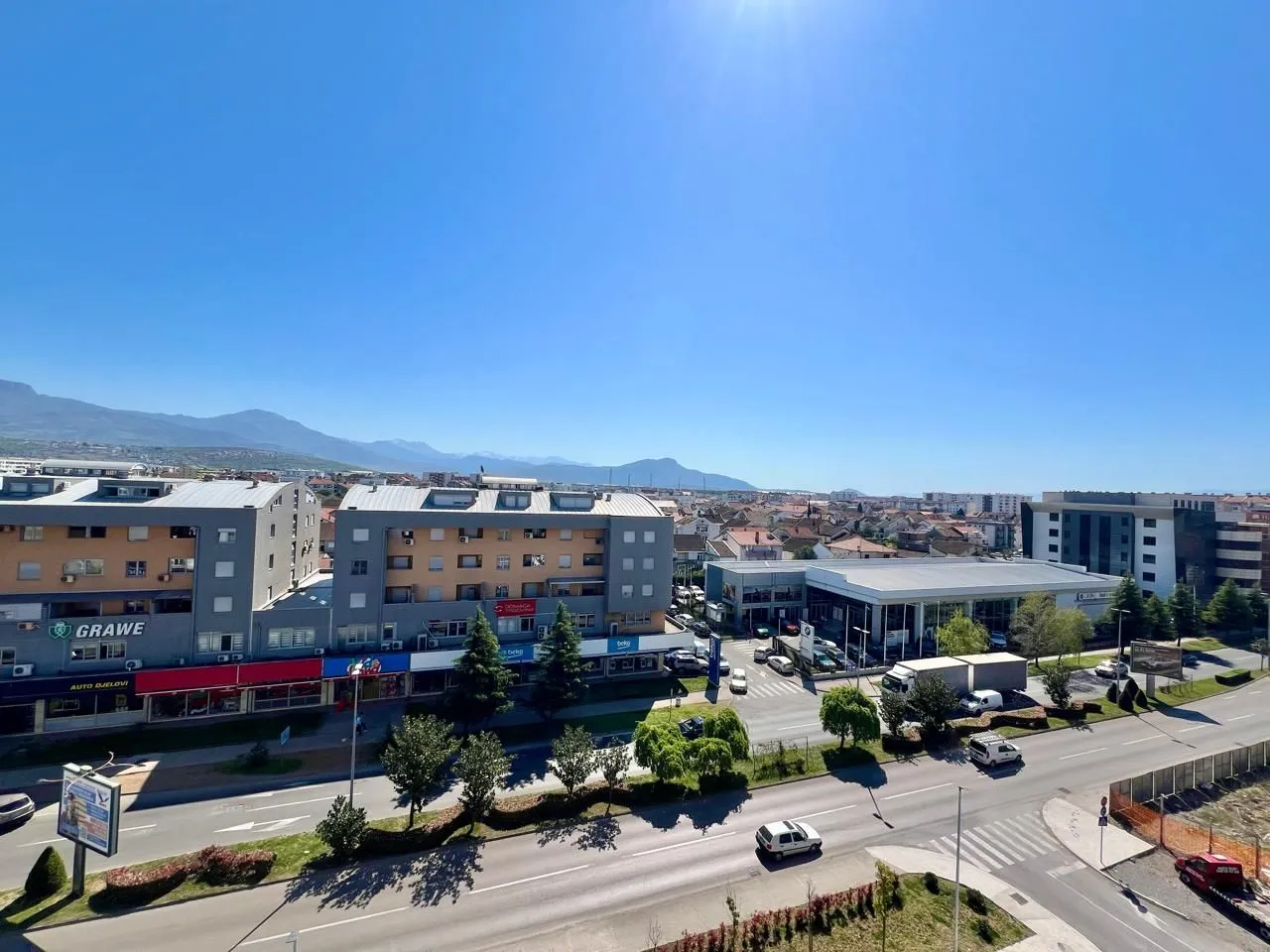 Pogled sa terase na okolne zgrade, ulicu i planine u daljini.