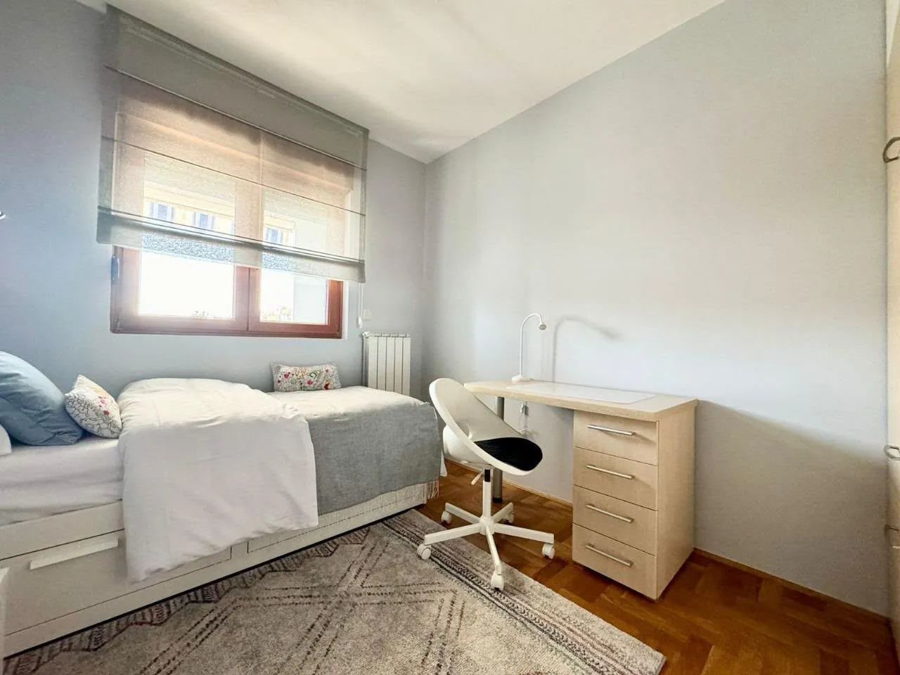Furnished bedroom with a bed, desk, and window.
