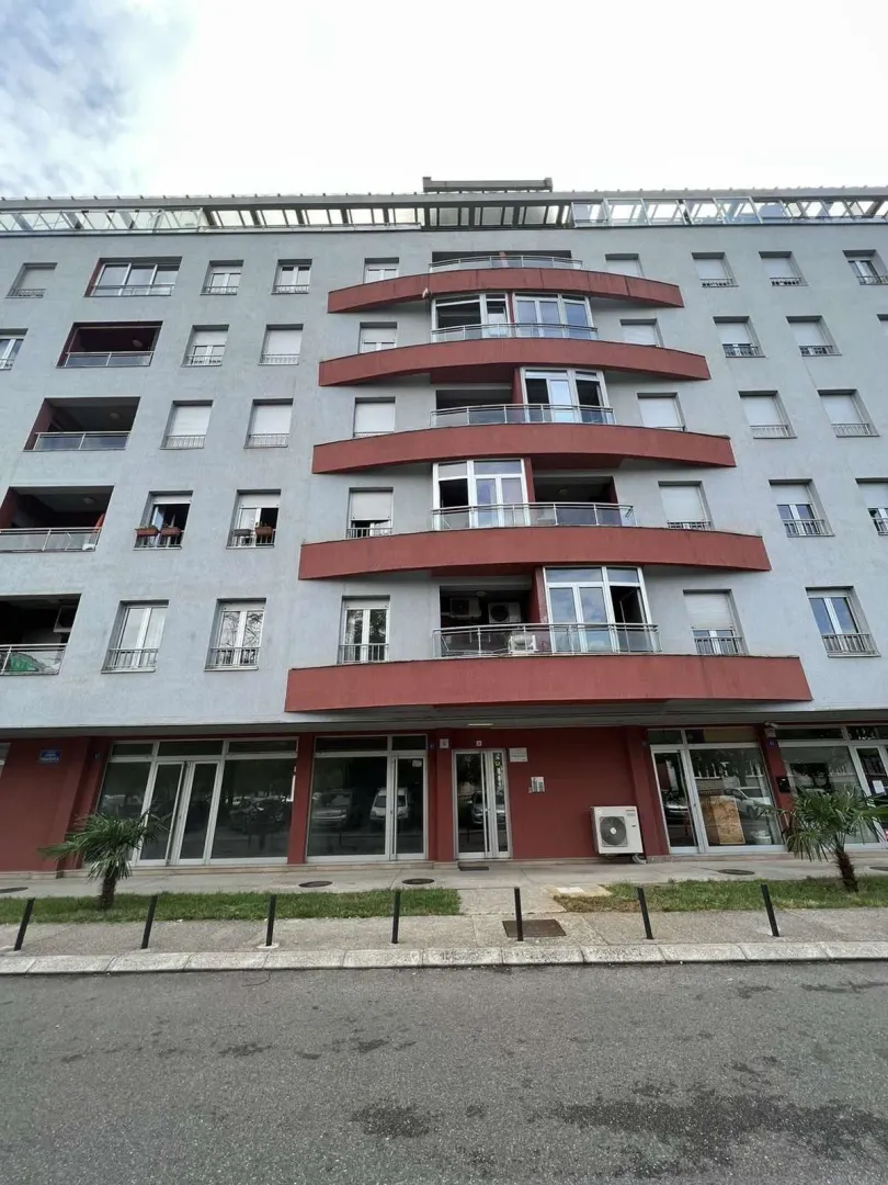 Vanjski izgled višespratne stambene zgrade sa crvenim balkonima.