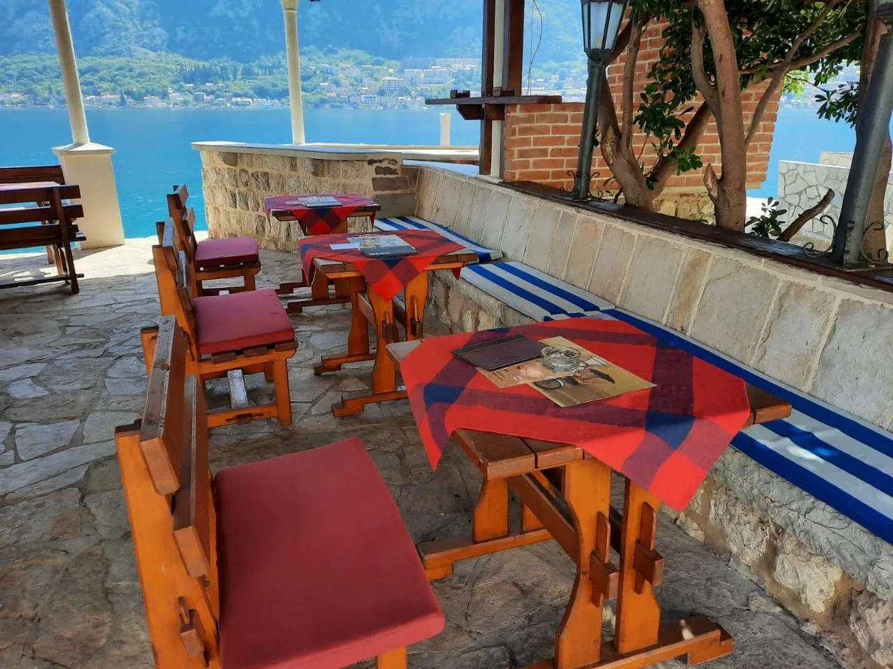Natkrivena terasa restorana sa drvenim stolovima i pogledom na more.