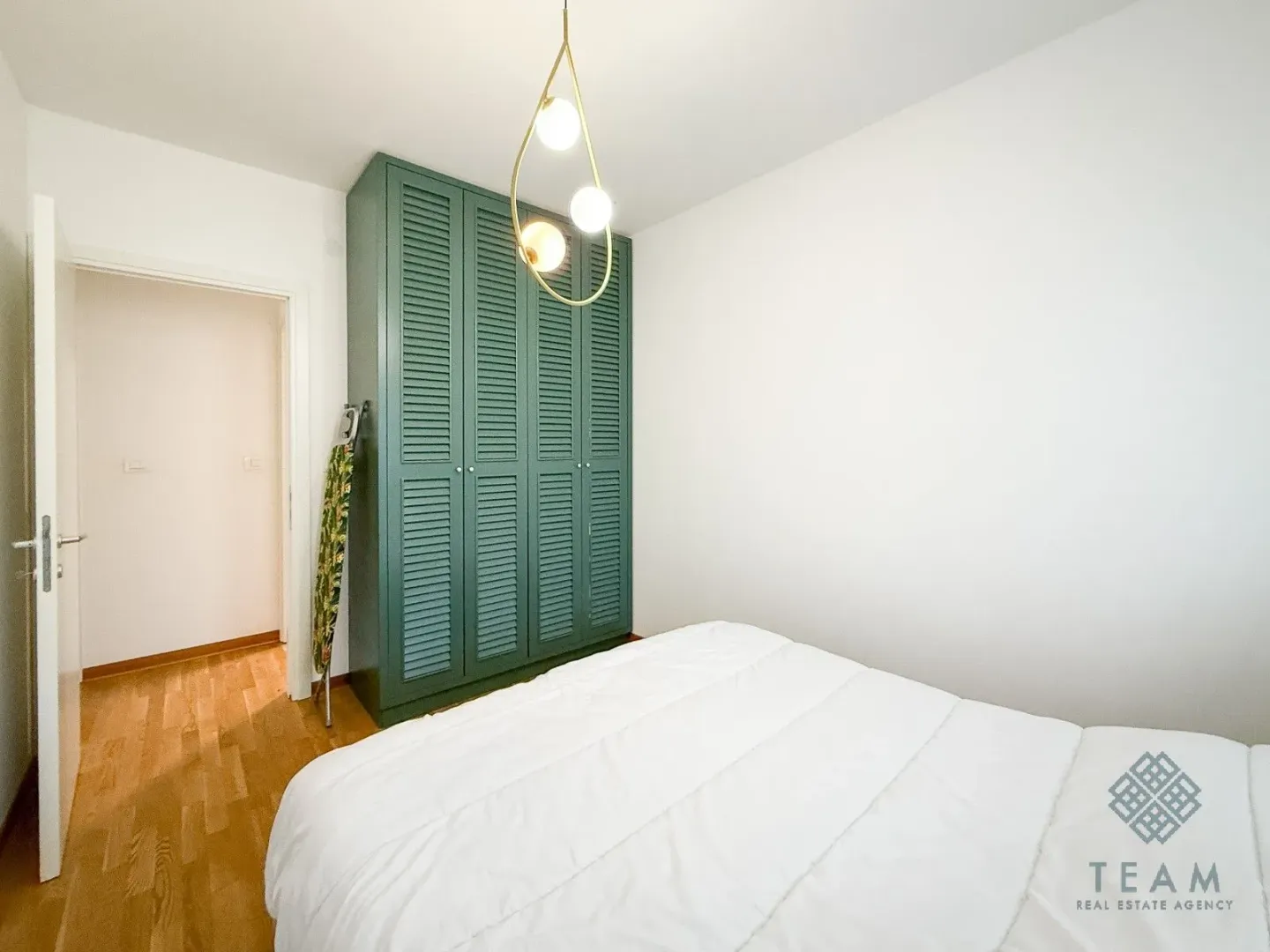 Spavaća soba sa bračnim krevetom, zelenim garderoberom i modernim visećim lusterom.