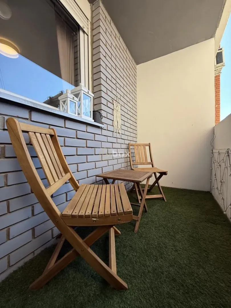 Small balcony furnished with wooden chairs and artificial grass.