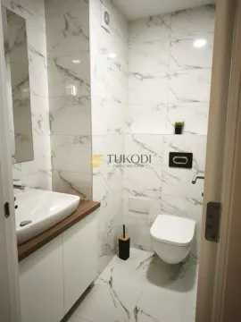 Small bathroom lined with marble-pattern ceramic tiles, featuring a basin and toilet. - image 4