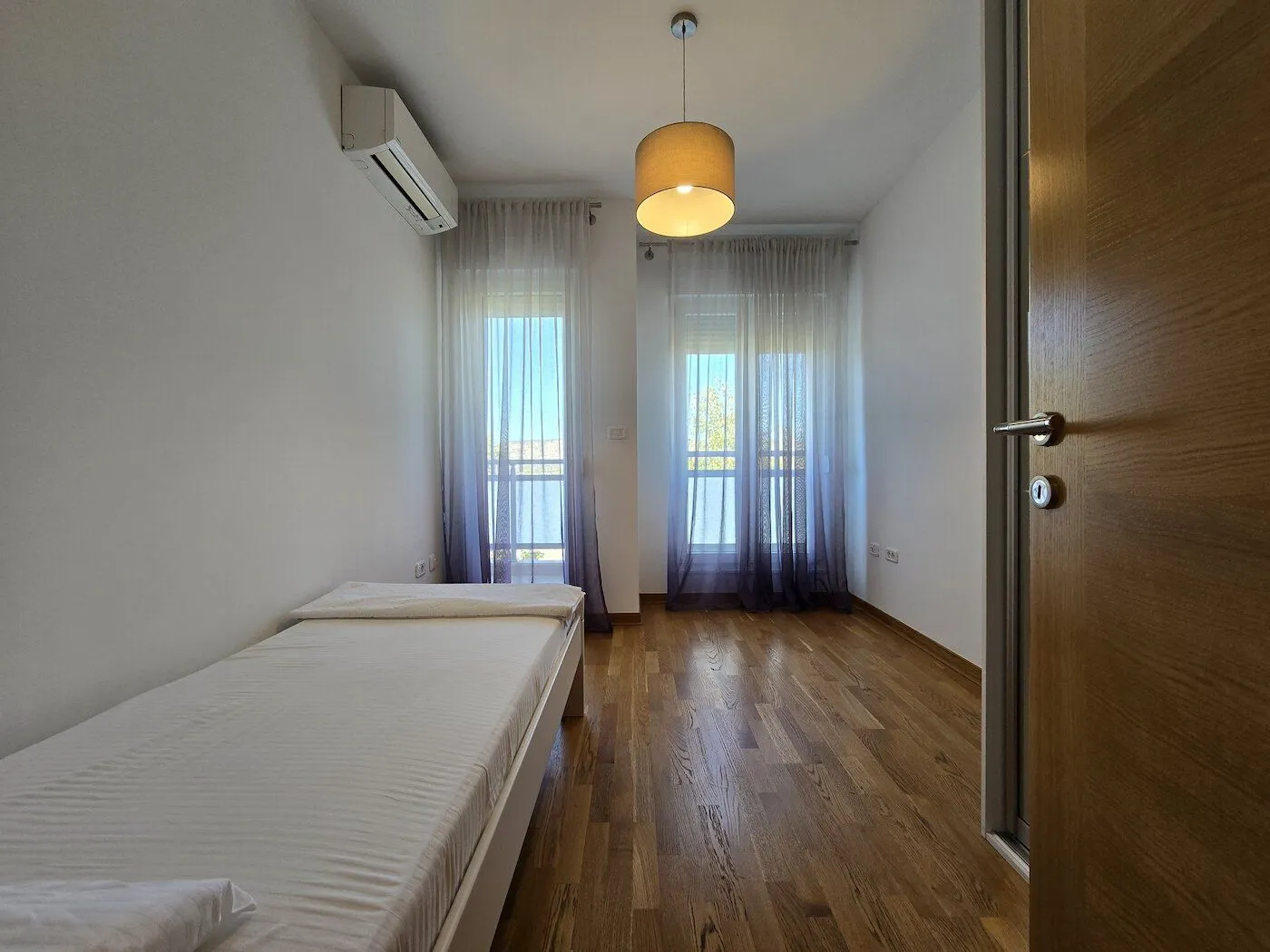 Svjetla spavaća soba sa krevetom i drvenim podom.