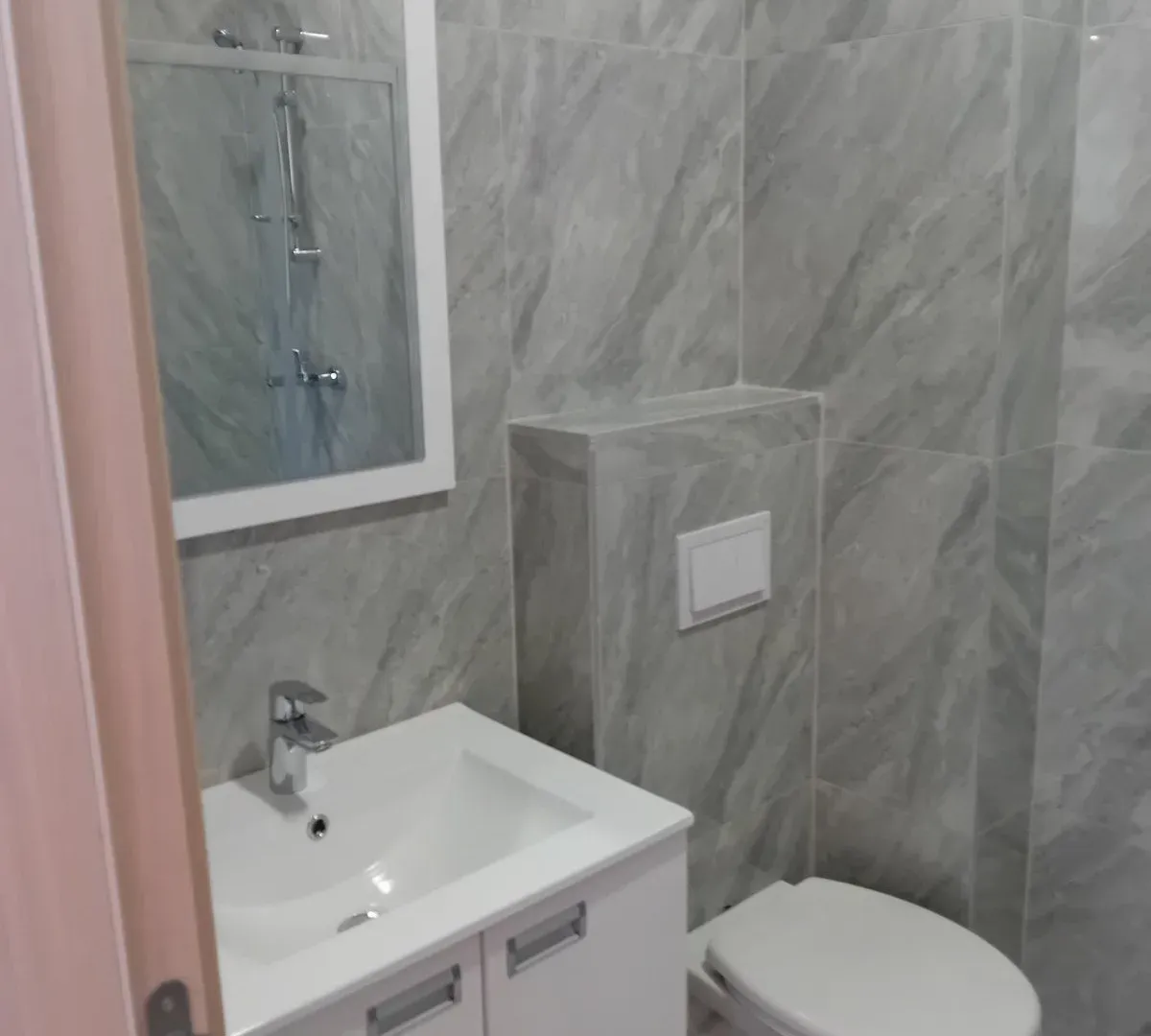 Modernly equipped bathroom with a washbasin, mirror, and toilet bowl.
