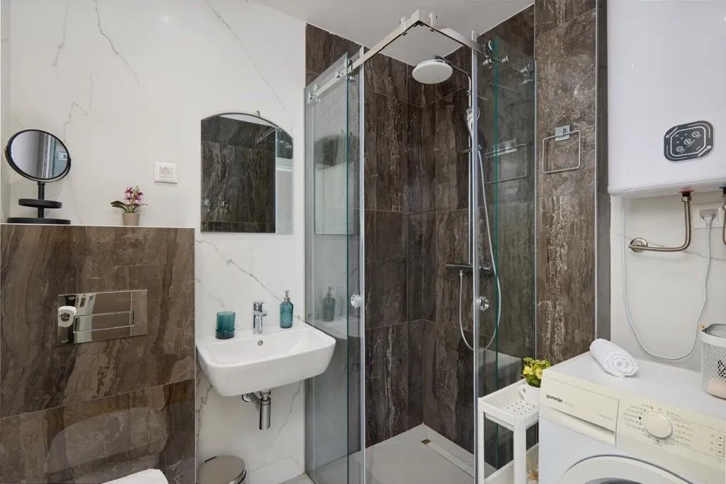 Modern bathroom with a walk-in shower, washbasin, and washing machine.