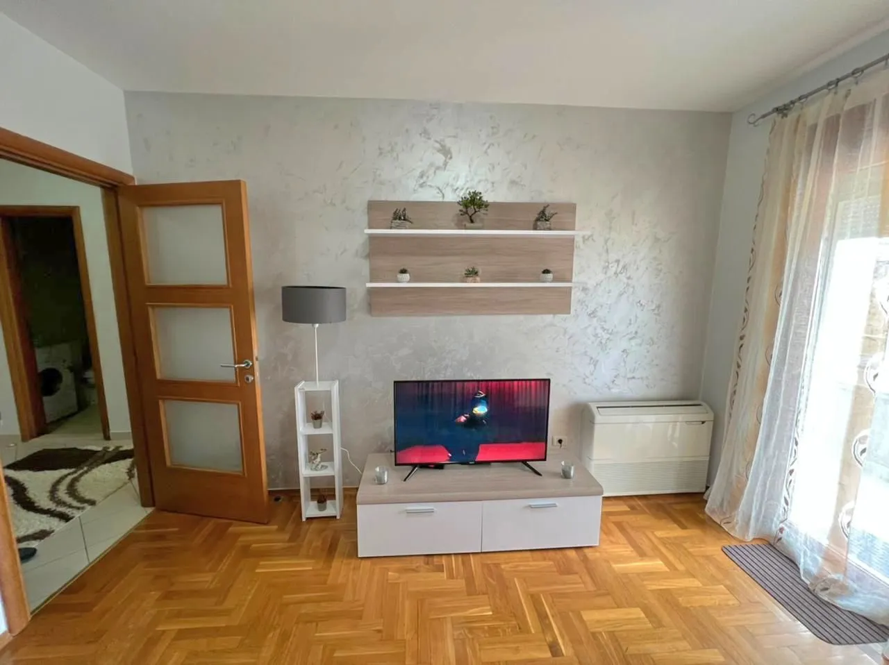 Dnevna soba sa televizorom, drvenim podom i policama na zidu.