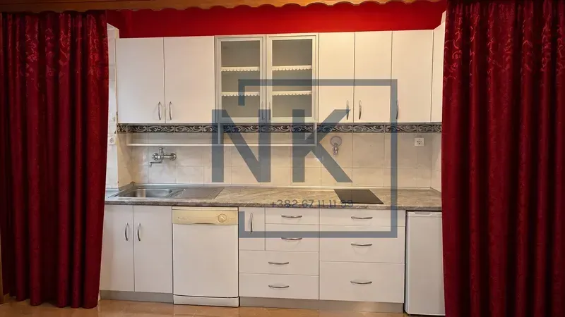 White kitchen with a sink, built-in cooktop, and cabinetry framed by red curtains.