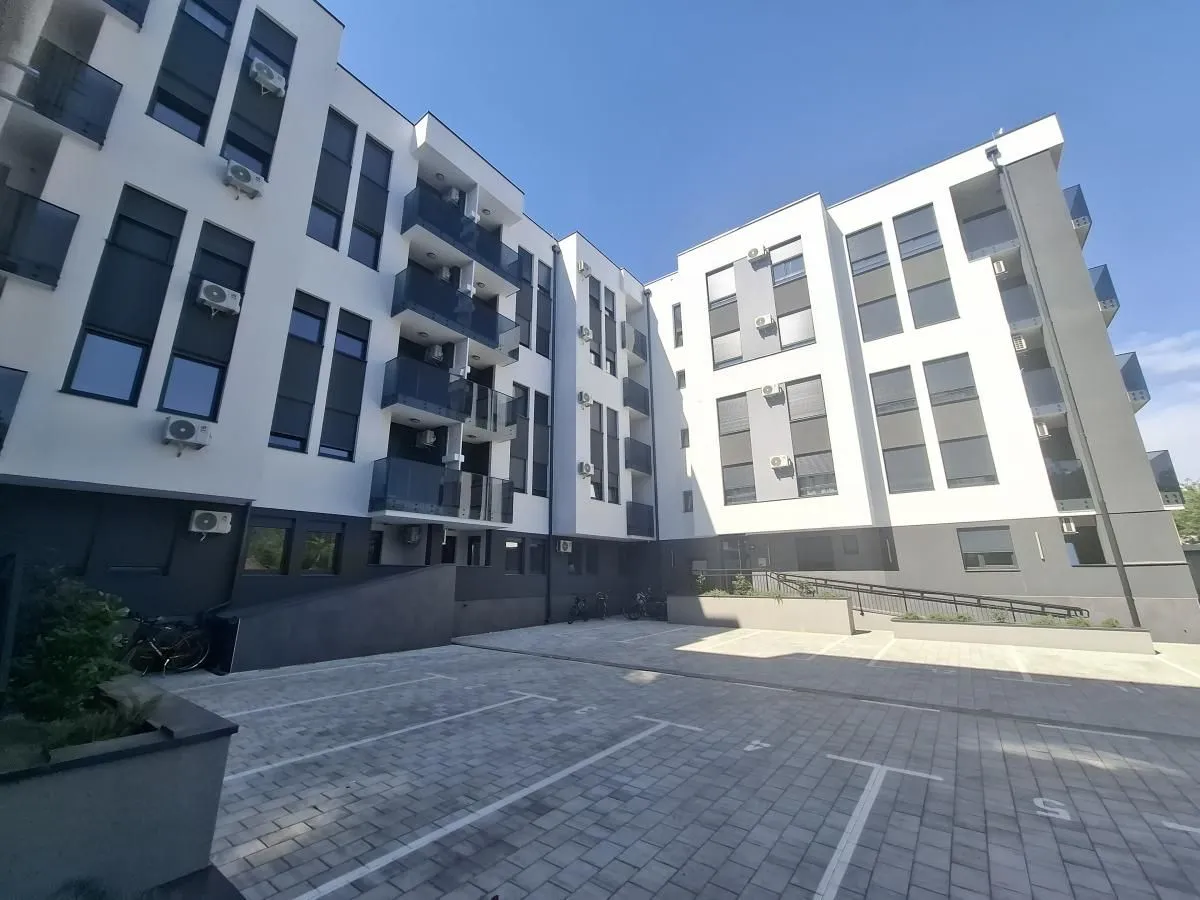 Pogled na fasadu moderne stambene zgrade sa parkingom u dvorištu.