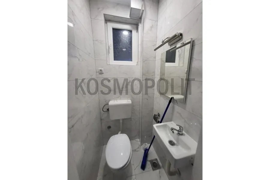 Small bathroom lined with marble tiles featuring a toilet, sink, and mirror.