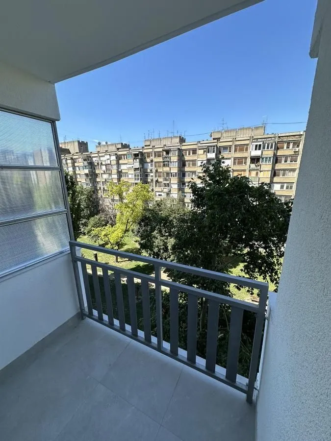Manji balkon sa pogledom na okolne zgrade i drveće.