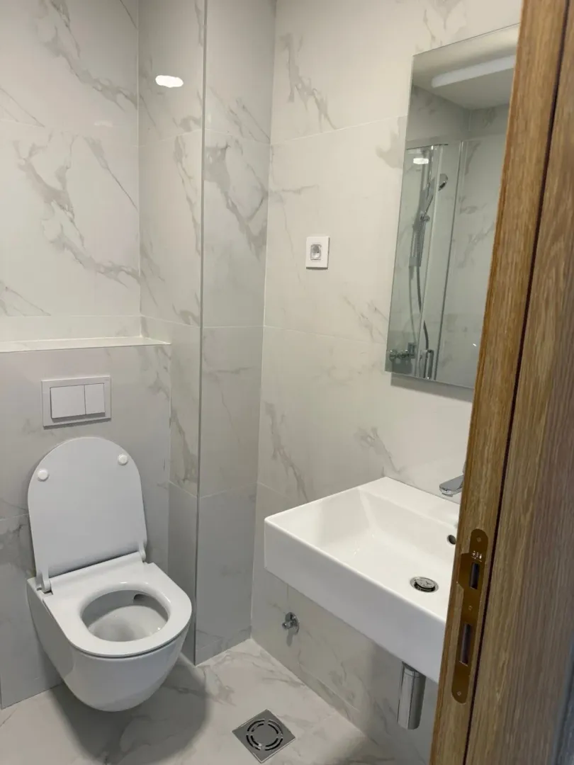 Savremeno opremljeno kupatilo sa bijelim pločicama i sanitarijama.
