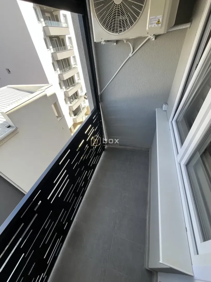 Manji balkon sa spoljnom jedinicom klima uređaja i pogledom na susedne zgrade.