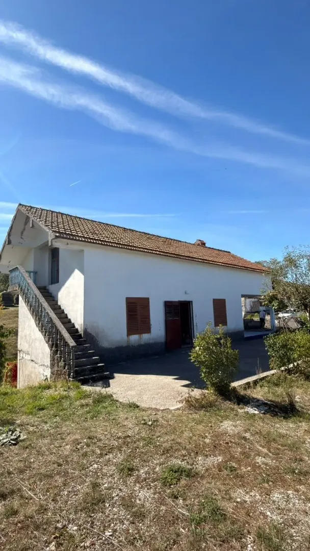 Eksterijer starije prizemne kuće sa spoljnim stepenicama i dvorištem.