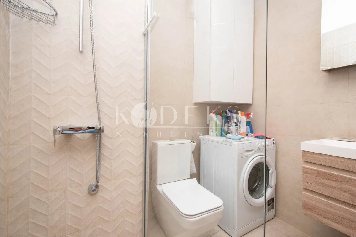 Modern bathroom equipped with a walk-in shower, toilet, washing machine, and vanity sink.