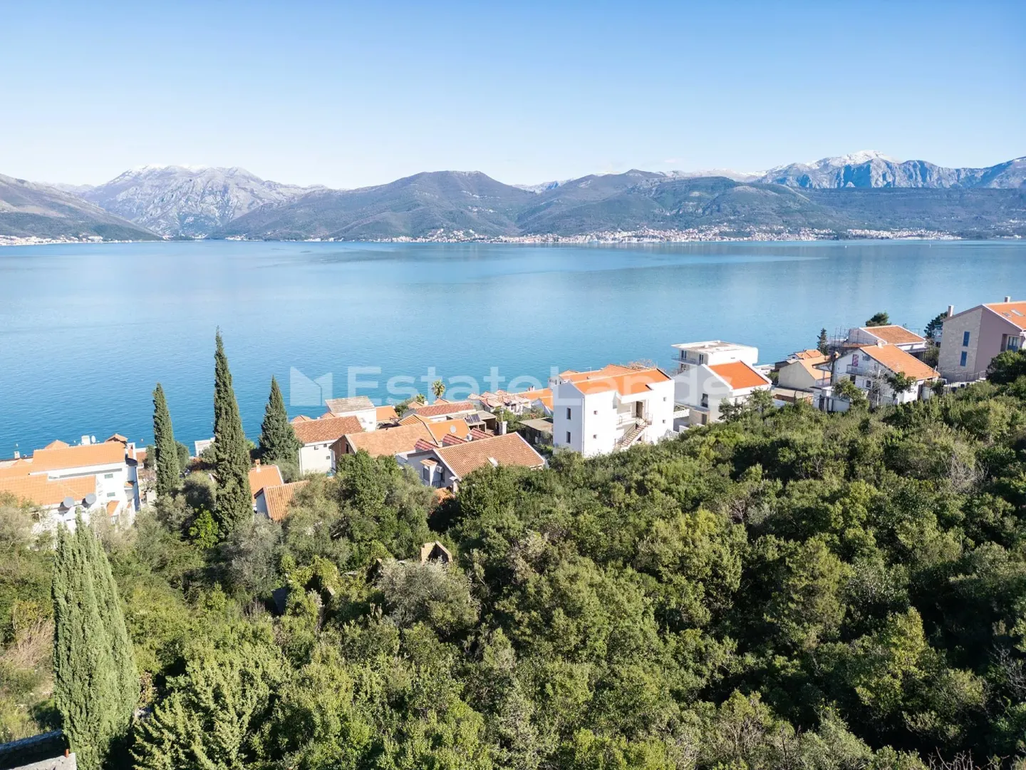 Pogled na more i okolno naselje sa zelenilom i planinama u pozadini.