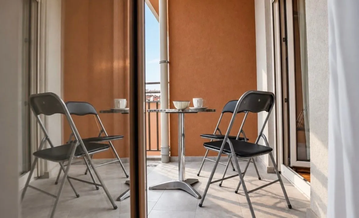 Manji balkon sa stolom i dvije stolice, djelimično prikazan kroz staklena vrata.