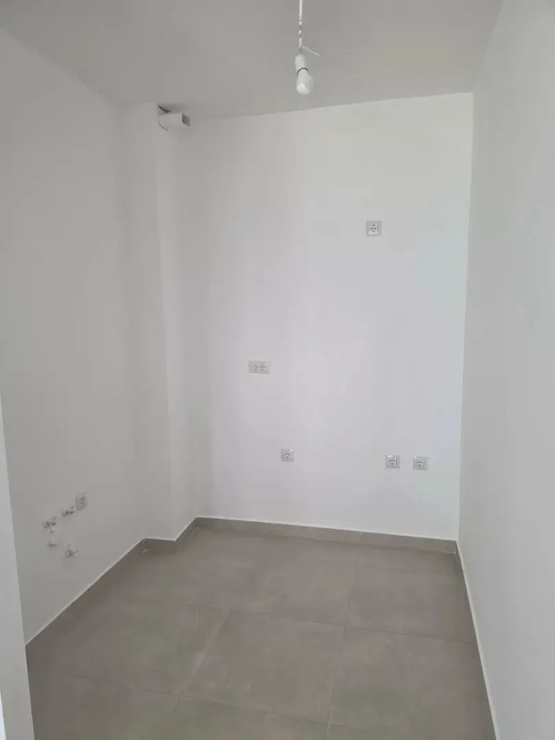 Prazna soba sa bijelim zidovima i sivim pločicama na podu.