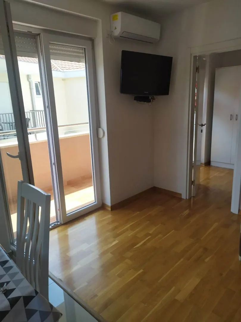 Manja dnevna soba sa drvenim podom, televizorom na zidu i izlazom na terasu.