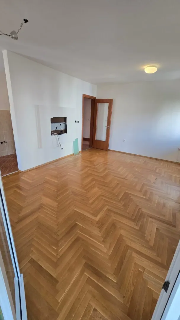 Prazna soba sa parketom i bijelim zidovima.