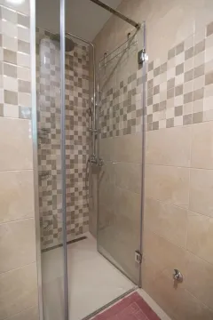 A modern shower cabin with glass doors and beige tiles. - image 9