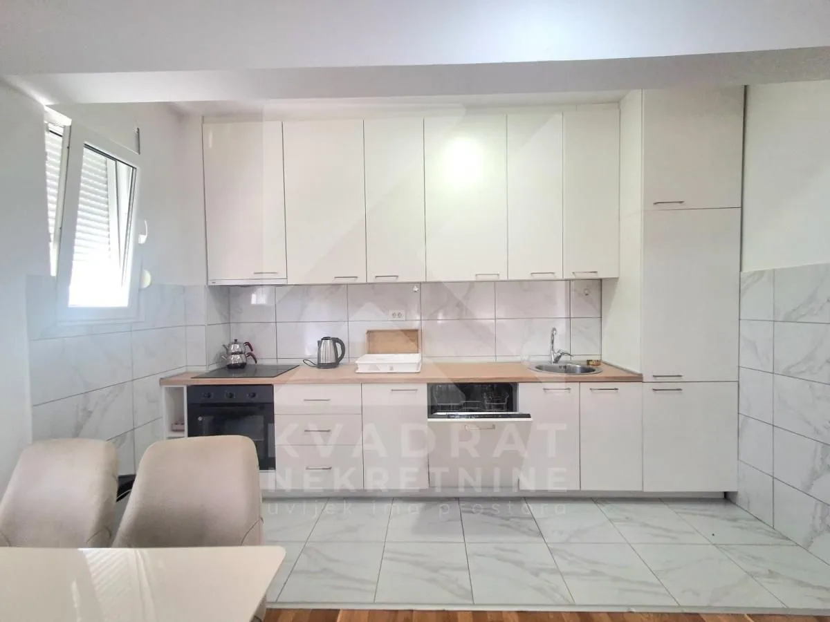 Moderna bijela kuhinja sa ugradnim aparatima i trpezarijskim stolom u prvom planu.