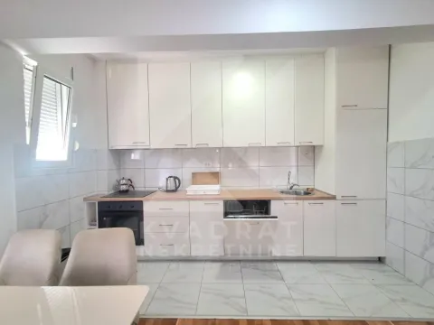 Moderna bijela kuhinja sa ugradnim aparatima i trpezarijskim stolom u prvom planu. - image 3