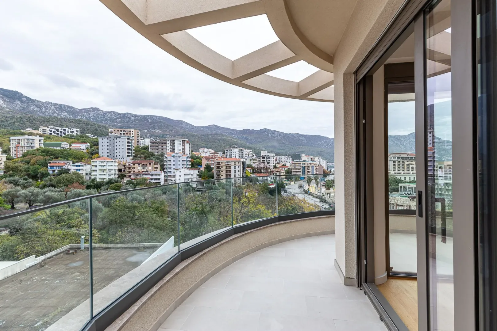 Spacious semicircular balcony with glass railing and views of the city and mountains.