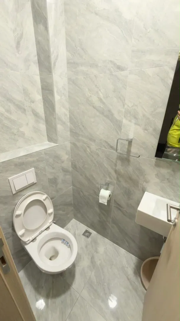 Manje kupatilo obloženo sivim mermernim pločicama sa wc šoljom i umivaonikom.