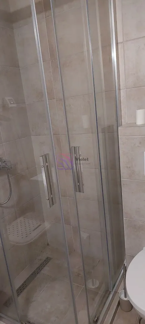 Moderne kupatilo sa tuš kabinom obloženom staklenim vratima.