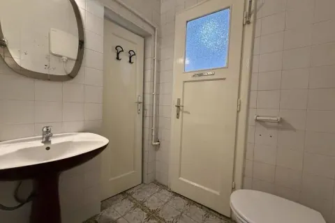 Smaller bathroom lined with white tiles featuring a sink and a toilet. - image 7