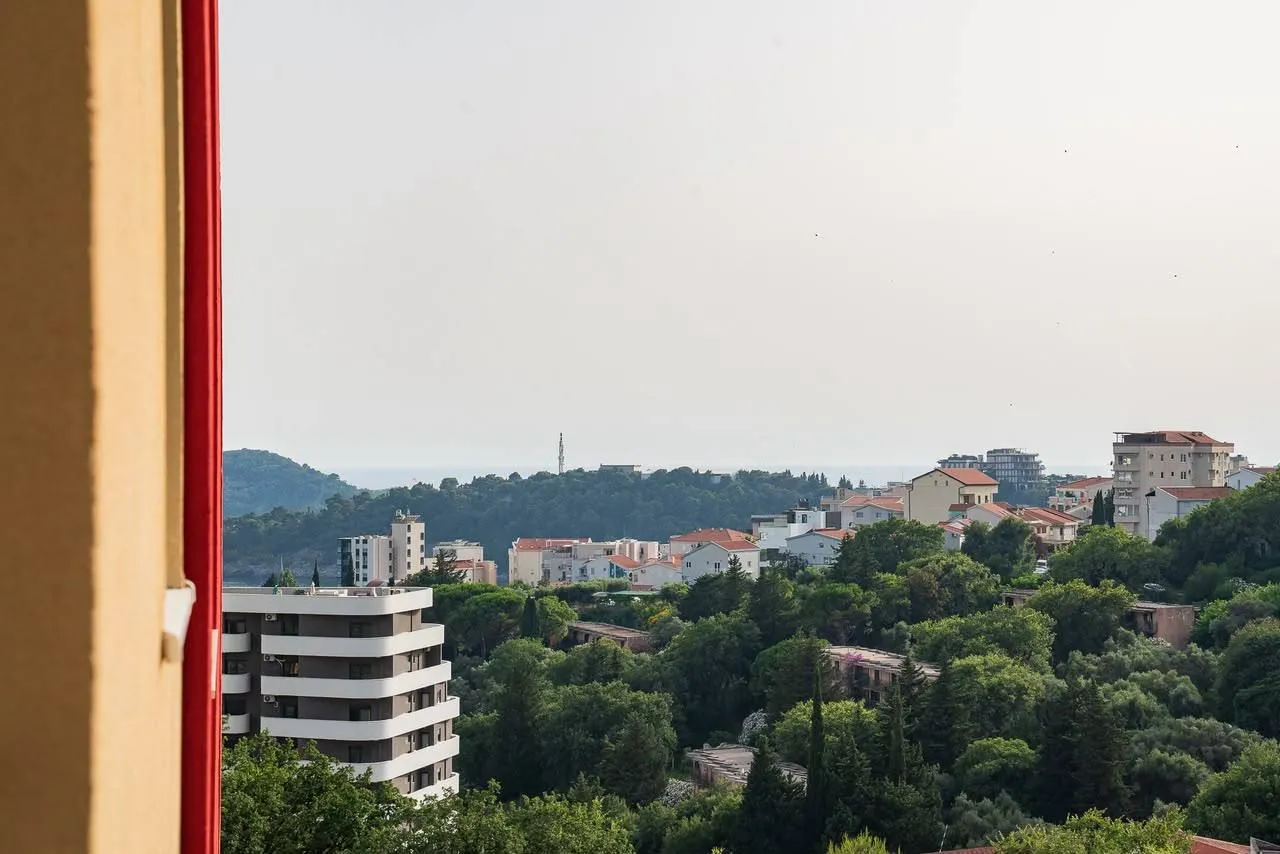 Pogled sa terase na naselje, zelenilo i more u daljini.