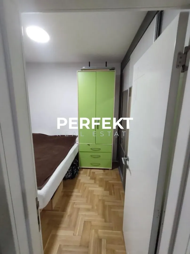 View from the hallway into a bedroom with a bed and a green wardrobe.