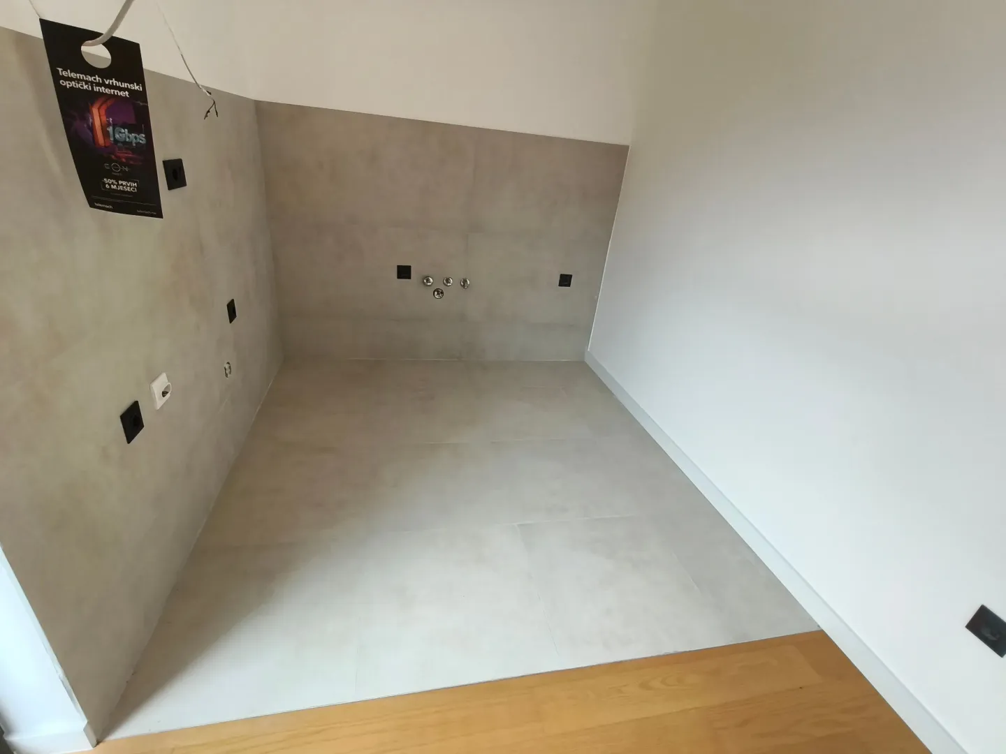 Prazna prostorija sa sivim pločicama i instalacijama na zidu.