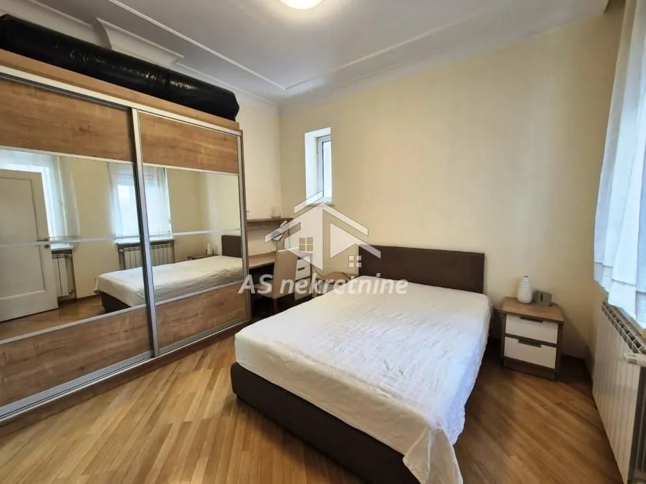 Furnished bedroom with a double bed, large mirrored wardrobe, and a desk.