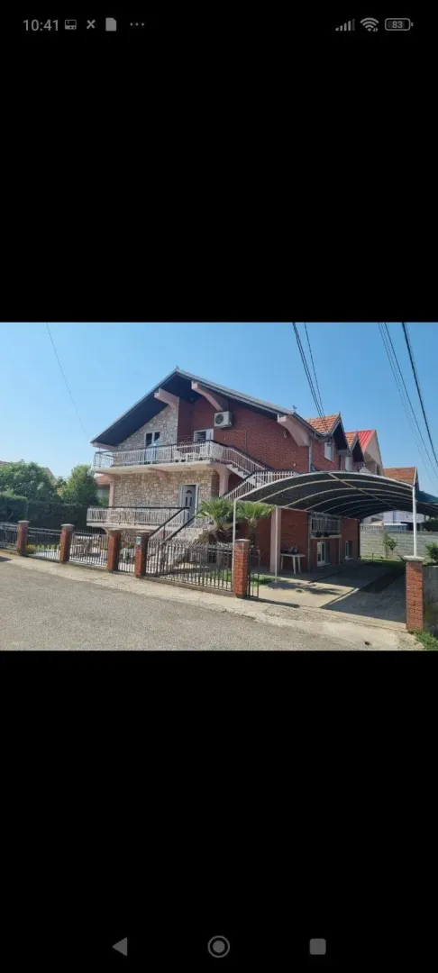 Exterior view of a two-story house with a fenced yard and a carport.