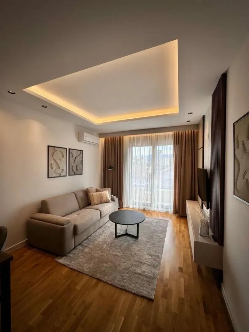 Dnevna soba sa garniturom, stočićem i modernim spuštenim plafonom sa rasvjetom.