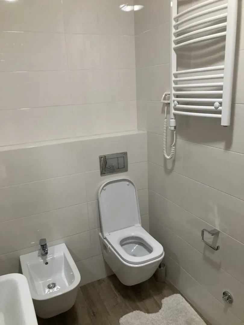 Modernly equipped bathroom with white tiles, toilet, bidet, and towel radiator.