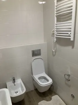 Modernly equipped bathroom with white tiles, toilet, bidet, and towel radiator. - image 7