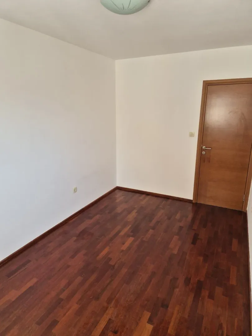 An empty room with dark parquet flooring and a wooden door.