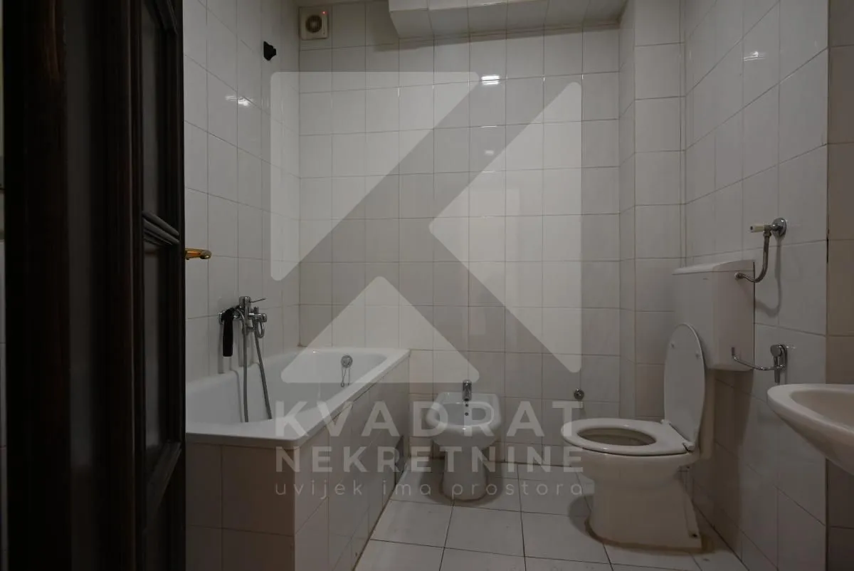 Bathroom lined with white tiles featuring a bathtub and a toilet.