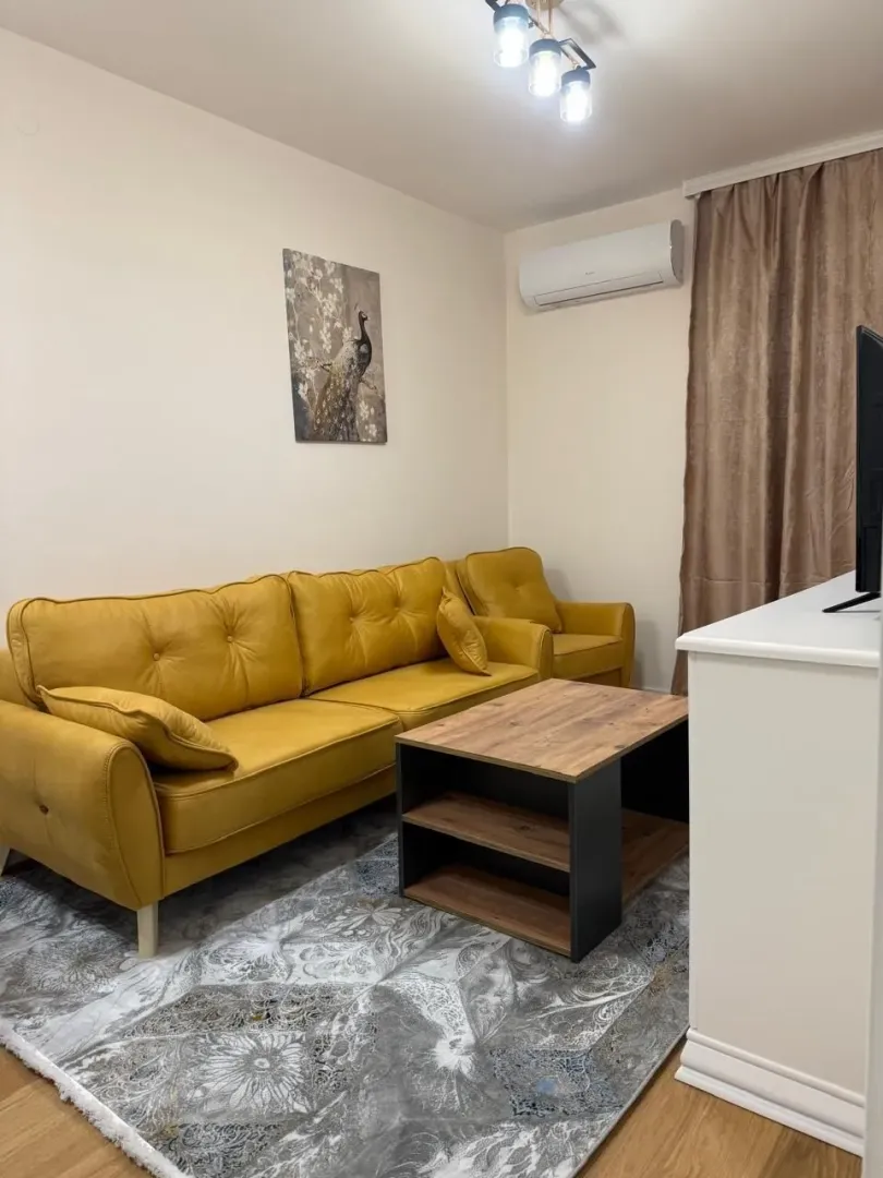 Svijetla dnevna soba sa žutom garniturom, drvenim klub stolom i tepihom.