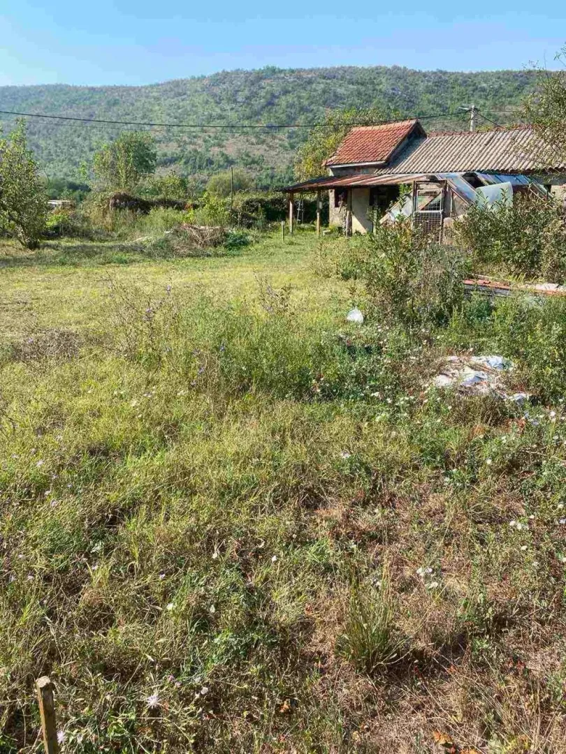Pogled na stariju kuću sa dvorištem i brdom u pozadini.
