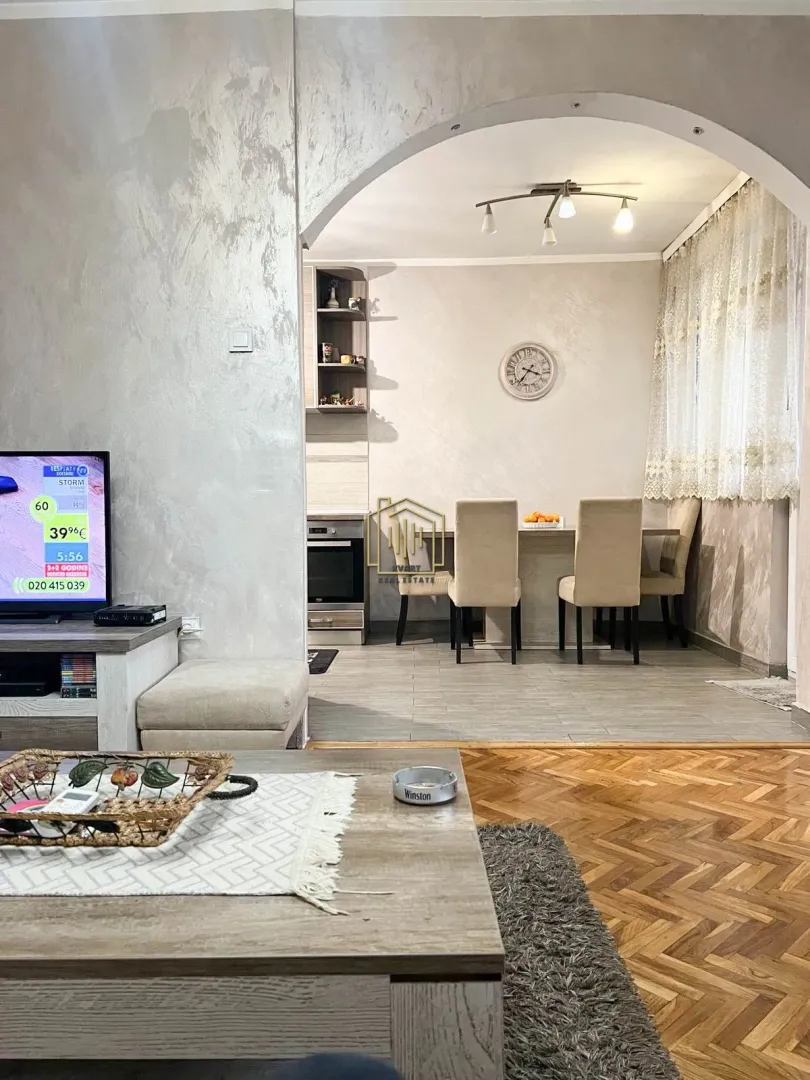 Pogled iz dnevne sobe prema trpezariji i kuhinji sa drvenim podom i lukom na prolazu.