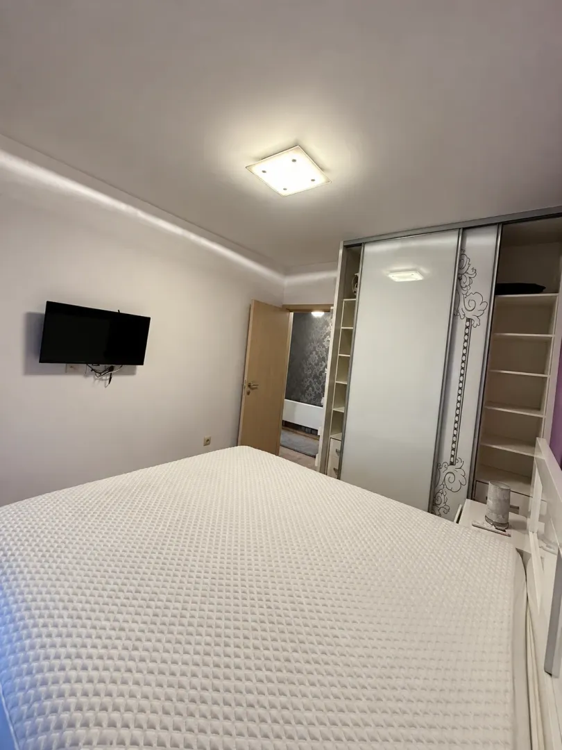 Spavaća soba sa bračnim krevetom, velikim garderoberom i zidnim televizorom.