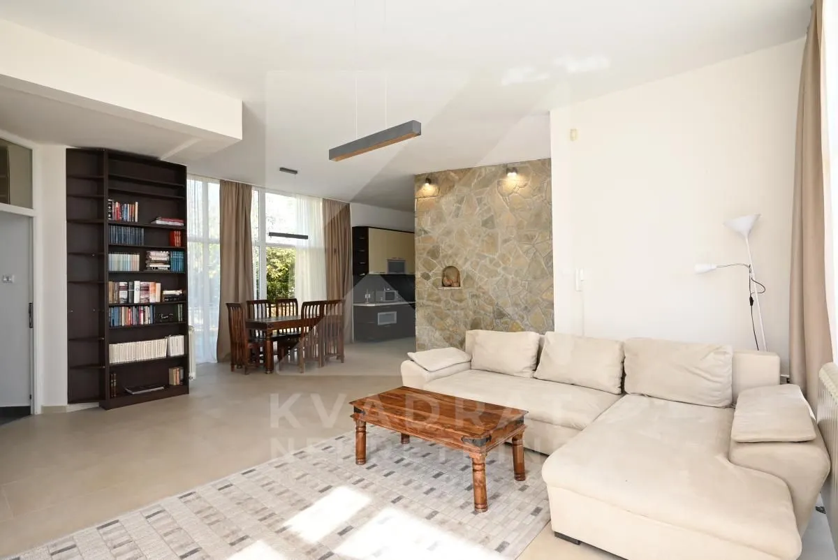 Spacious living room with a sofa, bookshelf, and dining area in the background.