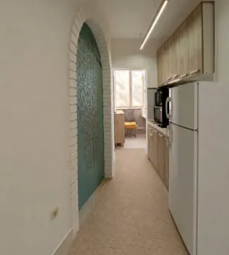 Manja kuhinja sa drvenim elementima, bijelim frižiderom i prolazom u pozadini. - image 6