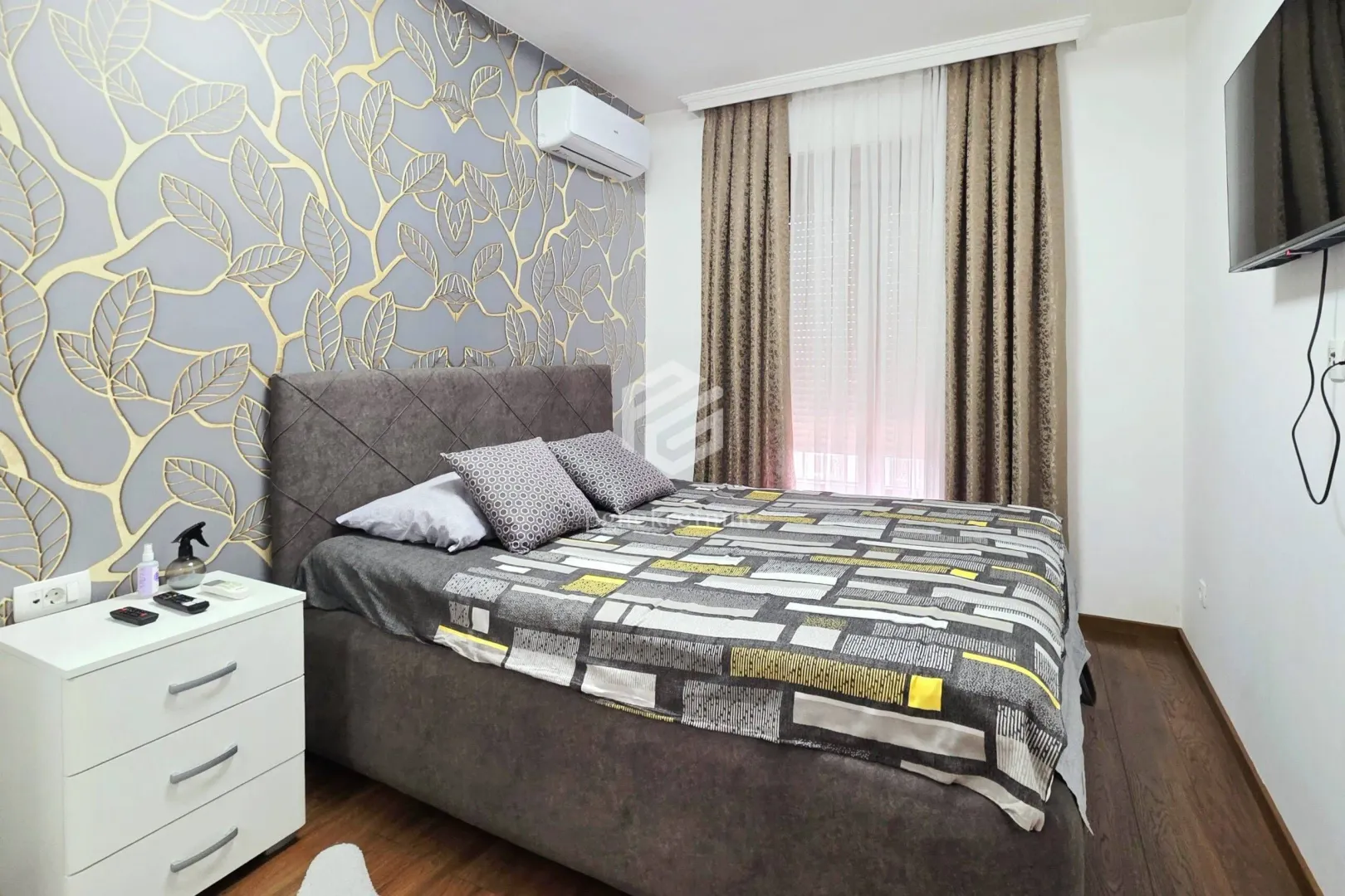 Furnished bedroom with a double bed, nightstand, and patterned wallpaper on the wall.