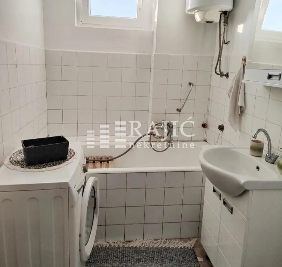 Smaller bathroom with a bathtub, washbasin, and washing machine.
